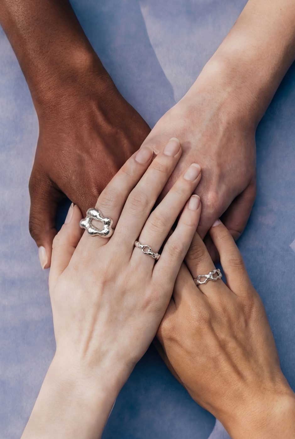 Stacked hands wearing silver rings on a lavender background