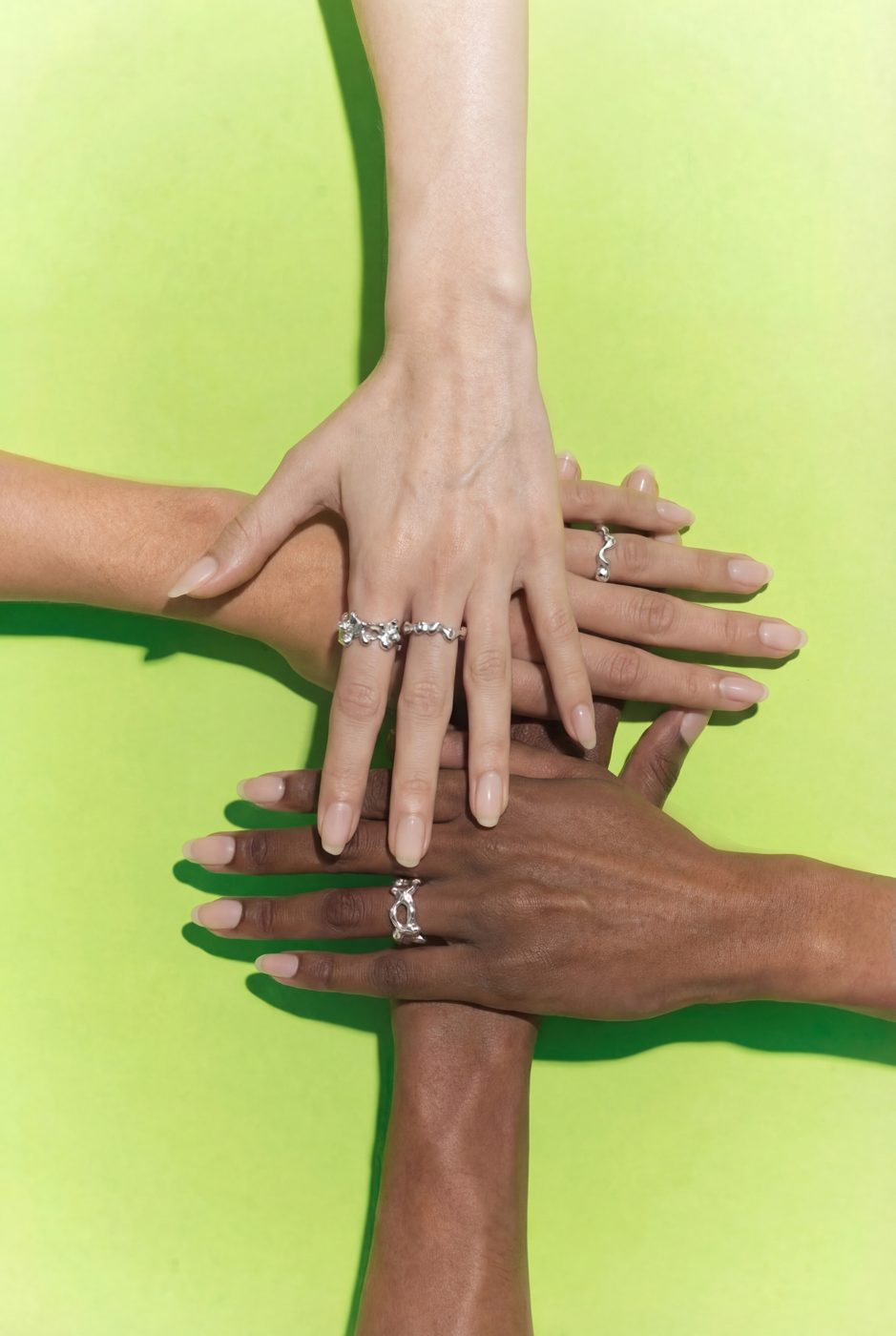 Four hands crossed on a lime background wearing silver rings